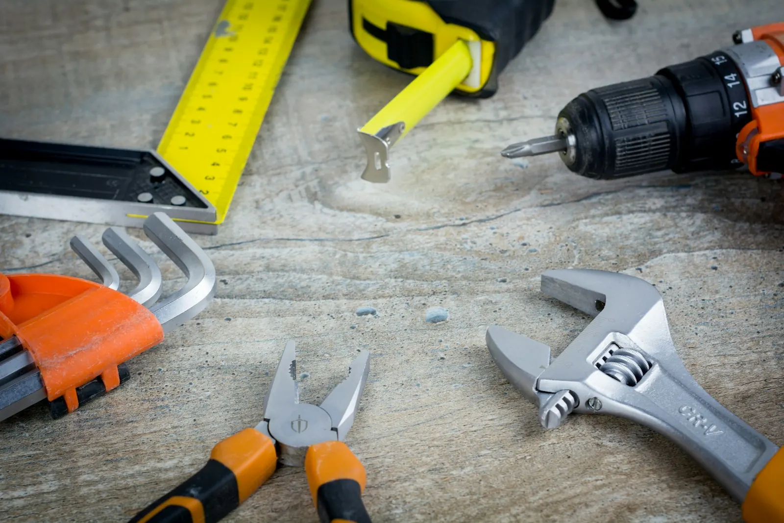 Tradie tools laid out on a workbench: drill, tape measure, spanner and pliers