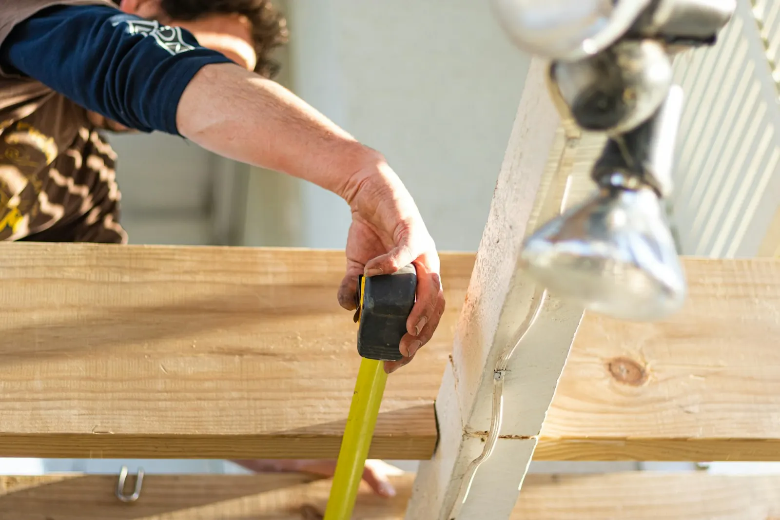 A builder measuring a length of timber with a tape measure