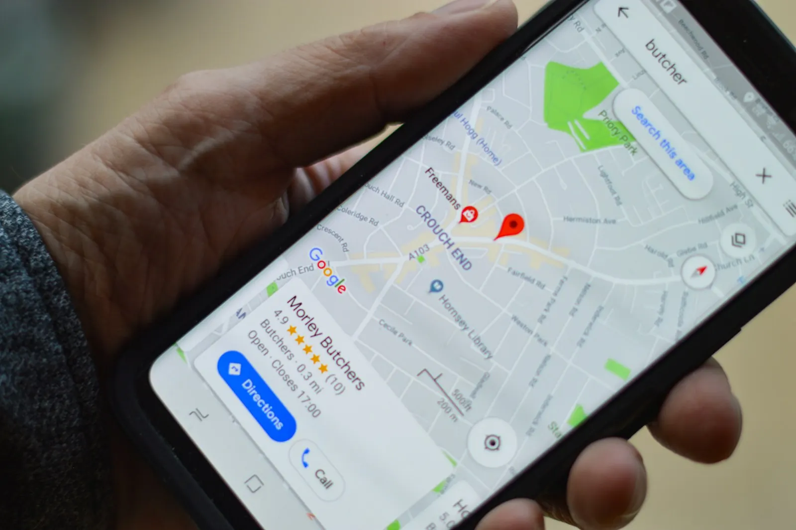 A hand holding a phone showing Google Maps business listings
