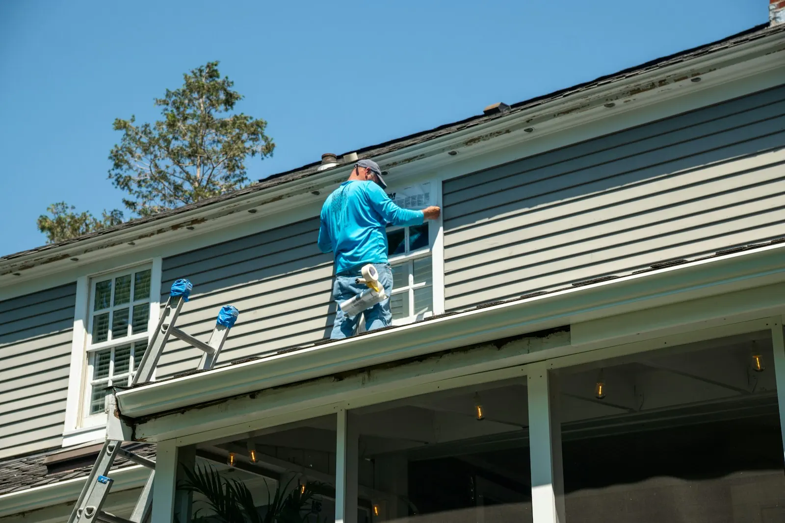 A tradesperson on a ladder working on the outside of a house