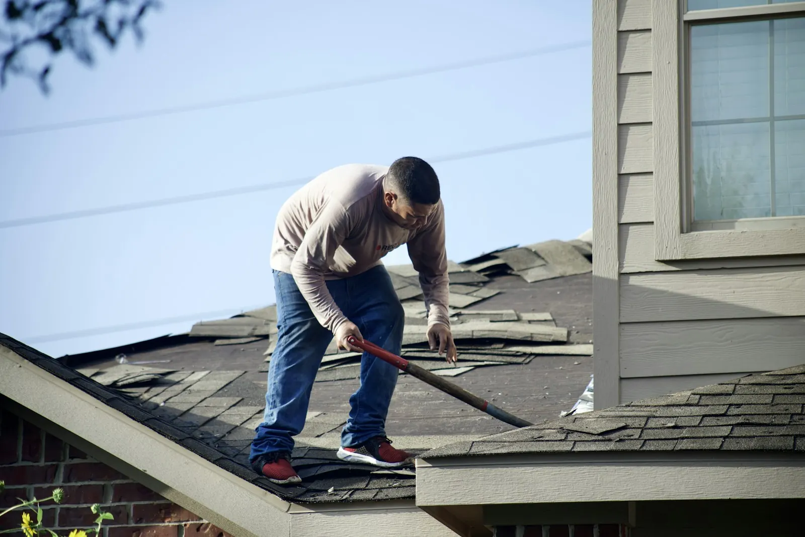A roofer removing old shingles from a house roof