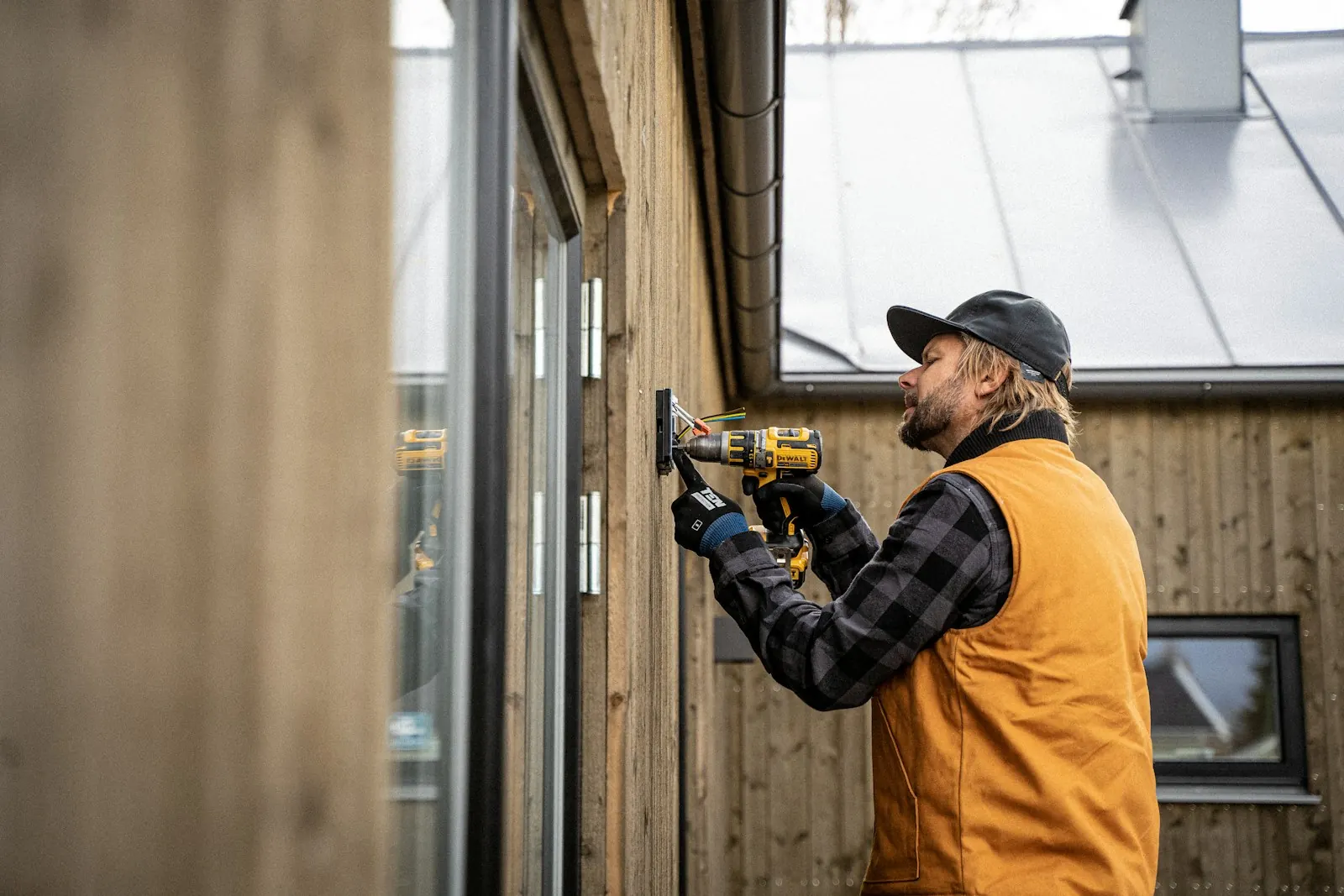 A tradesperson using a drill on the wall of a house