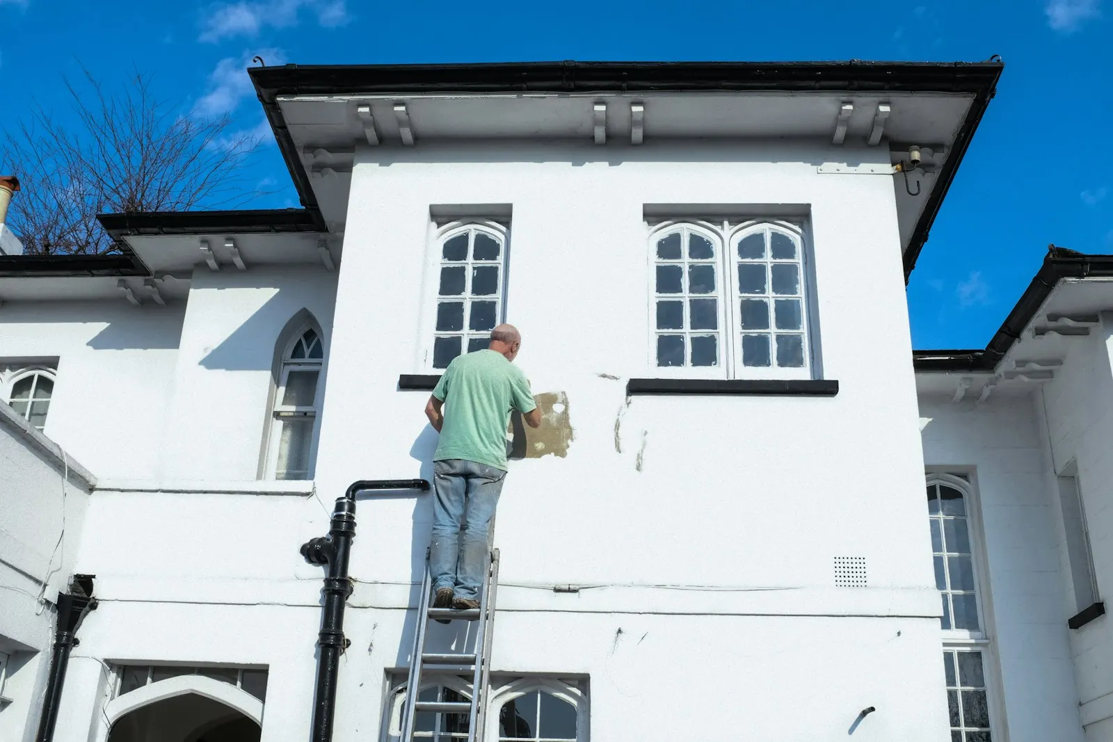 A painter on a ladder painting the outside of a house